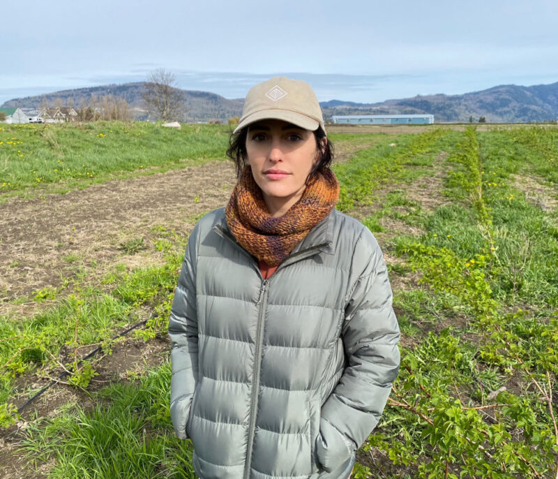 A photo of Shoshauna Routley standing in a grassy field wearing a beige baseball cap and quilted jacket.